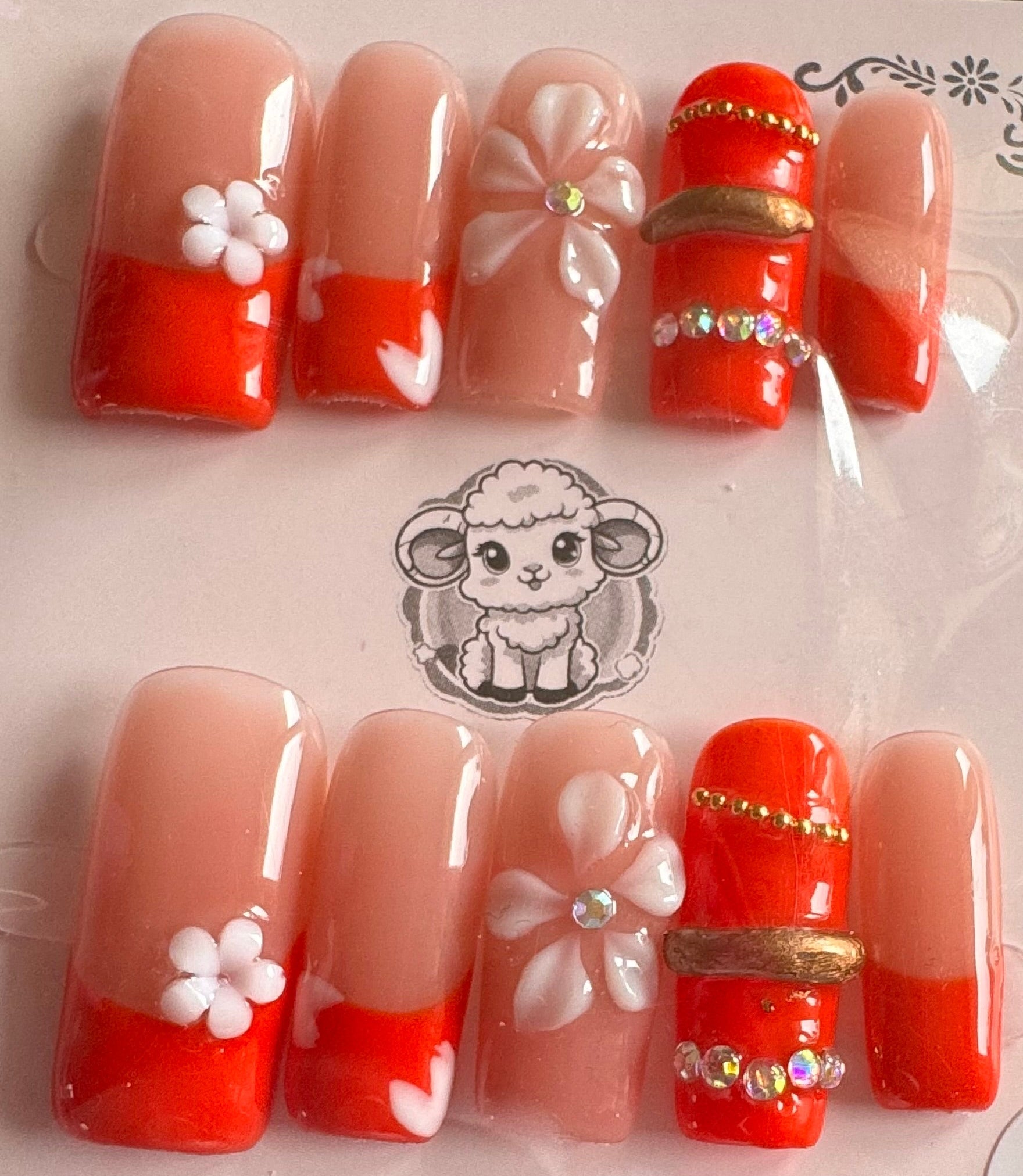 Set of red and orange false nails with decorative elements on a clear packaging.