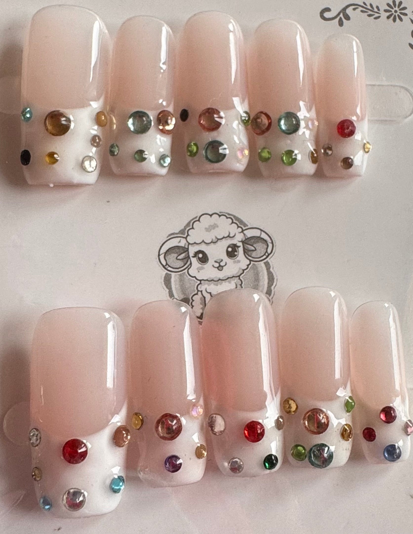 Set of false nails with colorful rhinestones on a packaging sheet.